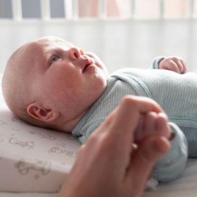 Bébé dans son berceau avec son tour de lit respirant et maman qui lui tient la main