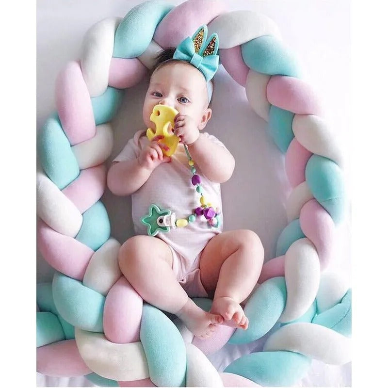 bébé qui joue avec hochet entouré d'une tresse de lit rose-bleu-blanche