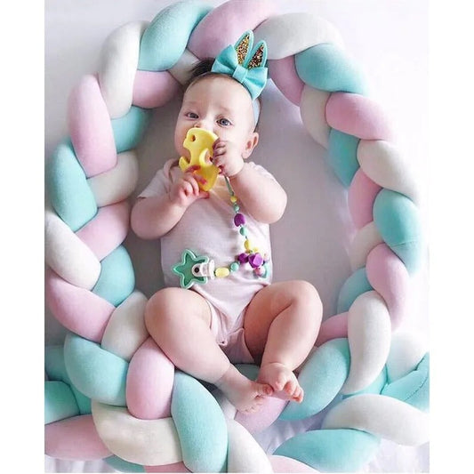bébé qui joue avec hochet entouré d'une tresse de lit rose-bleu-blanche