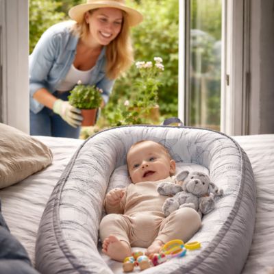 bébé éveillé dans son réducteur de lit dans salon et maman dehors qui surveille