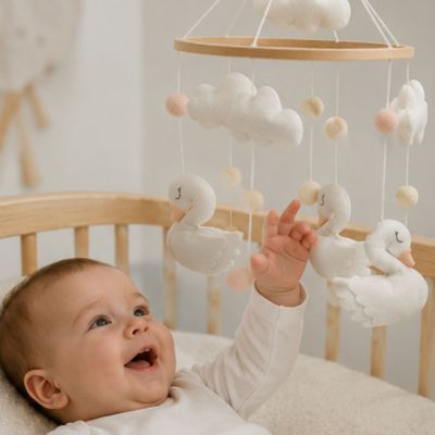 Bébé qui essai d'attraper son mobile lit bebe cygne blanc
