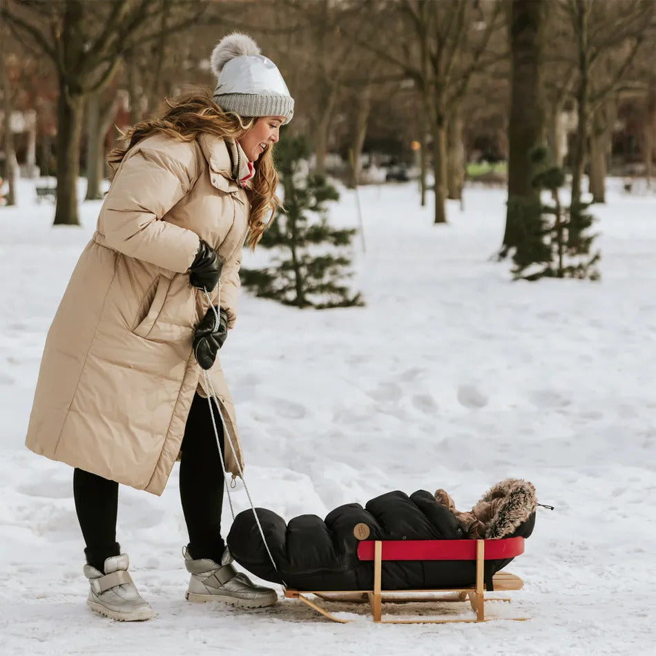 Chancelière-poussette- noir-en-flanelle-avec-bébé-dans-un-traineau-dans-le-parc-en-hiver-avec-maman