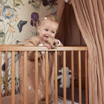 Petite fille sous son ciel de lit brun debout berceau souriante