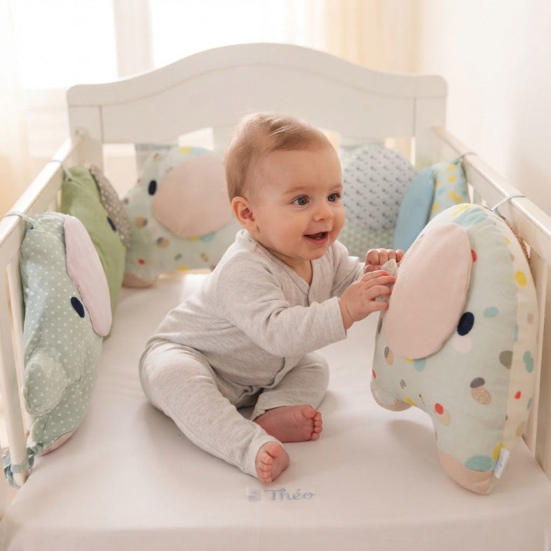 Théo qui, au réveil, observe et touche doucement son tour de lit bébé éléphant coloré