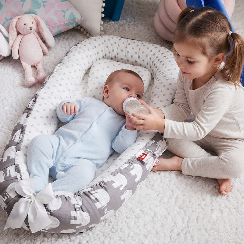 bébé dans son réducteur de lit bébé qui boit biberon avec l'aide sa soeur
