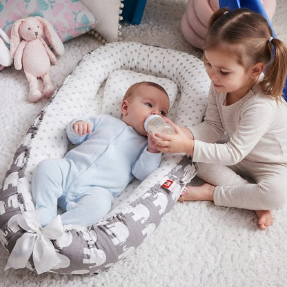 bébé dans son réducteur de lit bébé qui boit biberon avec l'aide sa soeur
