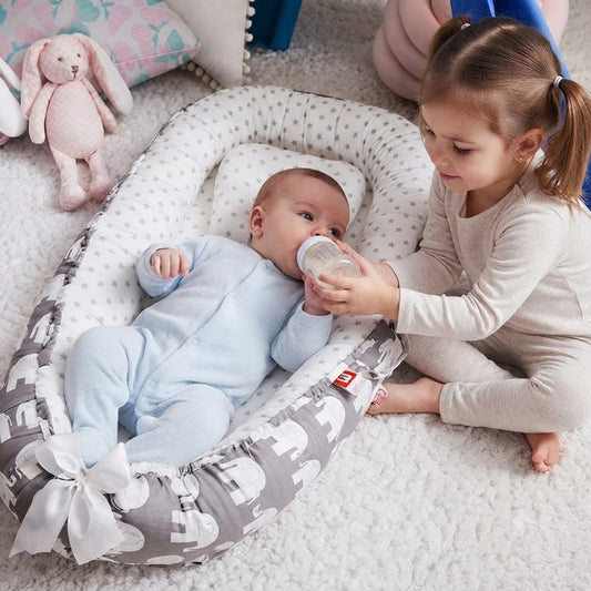 bébé dans son réducteur de lit bébé qui boit biberon avec l'aide sa soeur