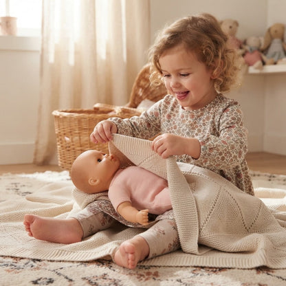 Fillette couvre sa poupée avec sa couverture bebe tricot