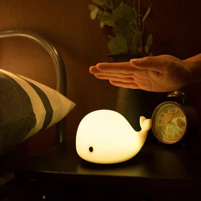 Veilleuse baleine sur table de chevet  avec une main qui s'apprête à taper.